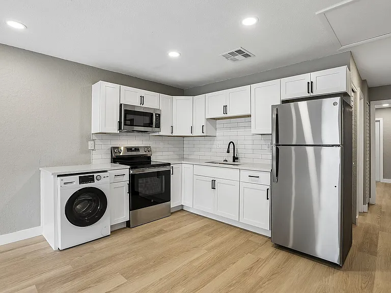 Modern kitchen with sleek stainless steel appliances, white cabinetry, and stylish wood flooring for a chic and functional design.