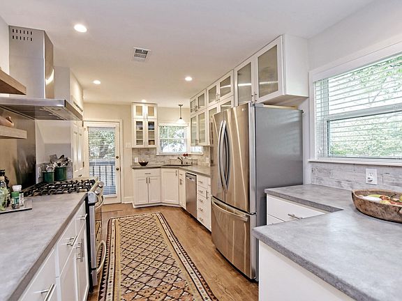 Recent kitchen with white cabinets, concrete counter tops, SS appliances including a gas range.