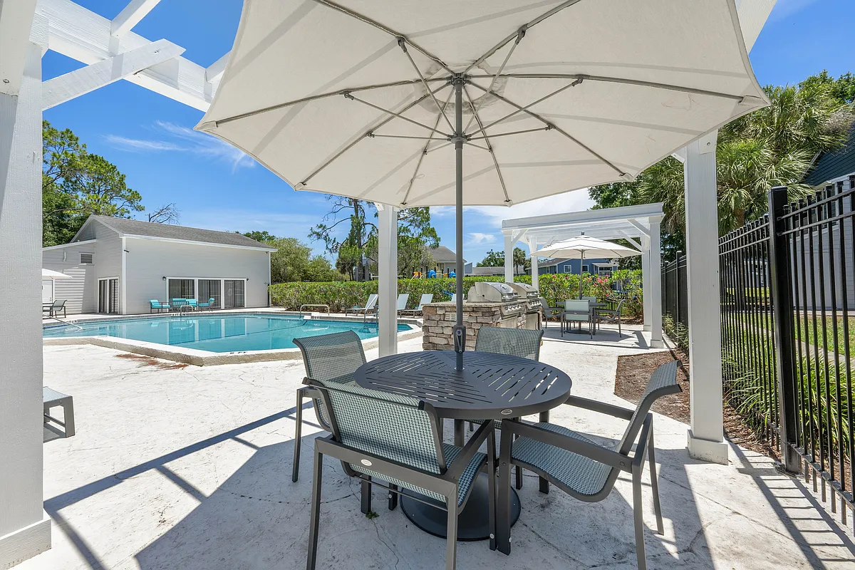 Inviting outdoor pool area featuring comfortable seating under umbrellas, modern grill, and lush greenery, perfect for relaxation and entertaining. - Vista North