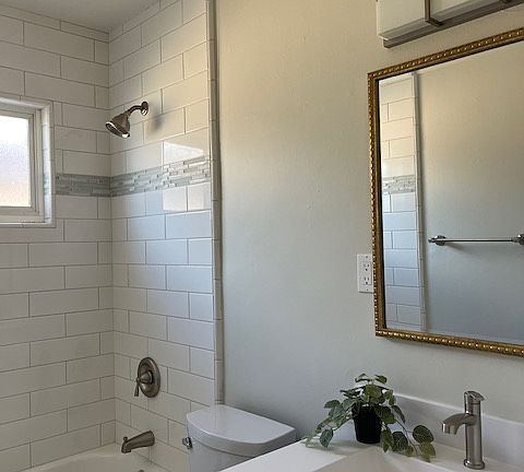 Beautiful bathroom with white tiles floors, gray shaker cabinet, white integrated sink, LED lighting, white subway tile tub/shower surround with marble/glass/tile accents, two tone paint.