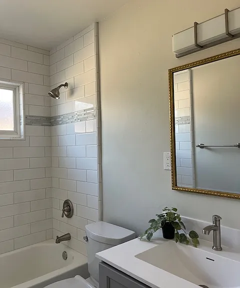 Beautiful bathroom with white tiles floors, gray shaker cabinet, white integrated sink, LED lighting, white subway tile tub/shower surround with marble/glass/tile accents, two tone paint.