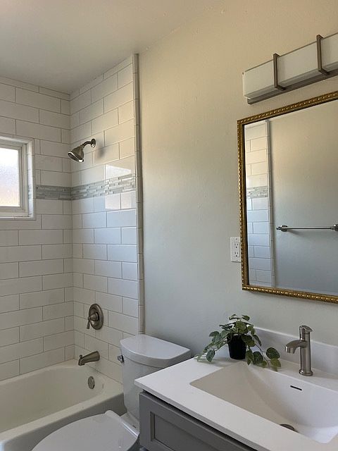 Beautiful bathroom with white tiles floors, gray shaker cabinet, white integrated sink, LED lighting, white subway tile tub/shower surround with marble/glass/tile accents, two tone paint.