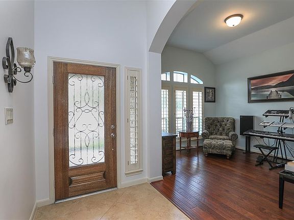 View inside entry toward front door: highlighting the archway into the Formal Living space with wood floors, coffered ceilings and lovely Plantation Shutters on windows that are topped by arched transom windows.