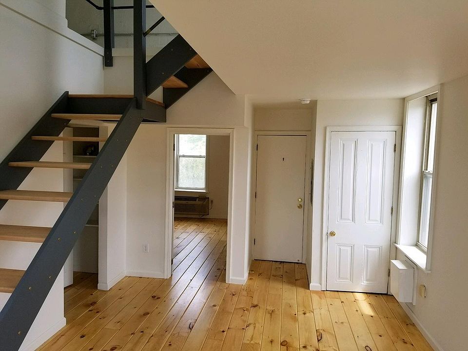 Living room looking toward apartment entry door and downstairs bedroom. Door on far right is coat closet. Under stairs on left is bathroom, laundry & linen closet.
