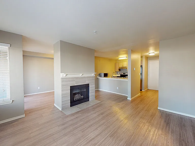 Apartment living room with wood-style flooring and a fireplace in select homes.