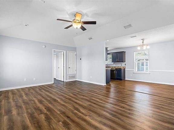 Unfurnished living room featuring dark wood-type flooring, vaulted ceiling, and ceiling fan with notable chandelier