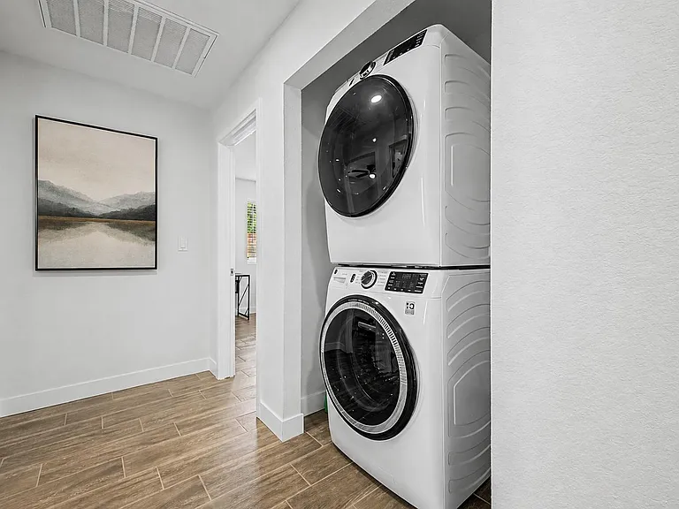 Hallway laundry nook with stacked front-load washer and dryer, offering convenient in-home laundry and easy access to nearby
