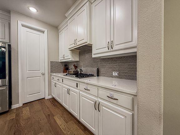 Spacious quartz counters shares gas cooktop with concealed hood range, convenient walk-in pantry, and raised panel key largo white cabinets
