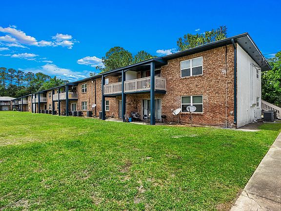 Charming brick apartment complex with spacious balconies, nestled in a serene green landscape under a clear blue sky.