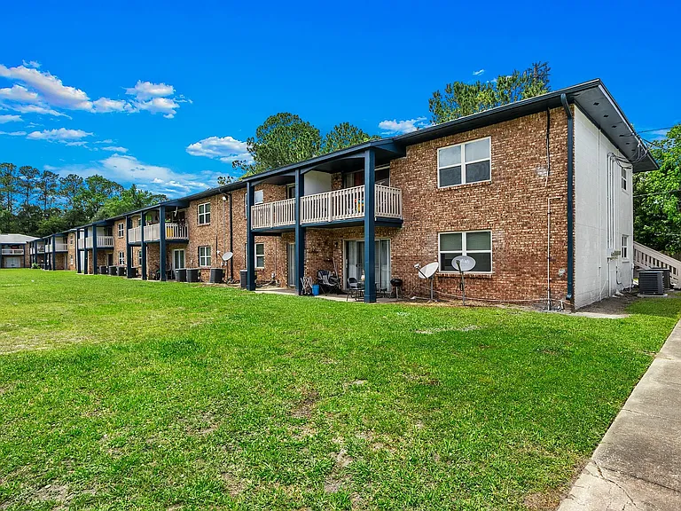 Charming brick apartment complex with spacious balconies, nestled in a serene green landscape under a clear blue sky.