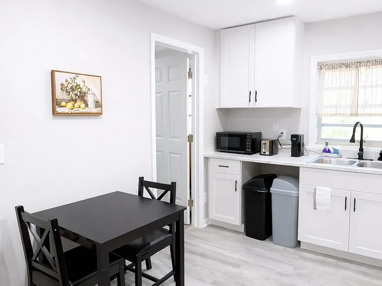 Eat-in kitchen with a two-seat dining set, ample white cabinetry, and a double-basin sink beneath the window.