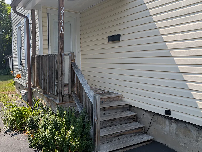 Exterior entrance with small porch. Black topped driveway for off street parking. Landscaped along porch.