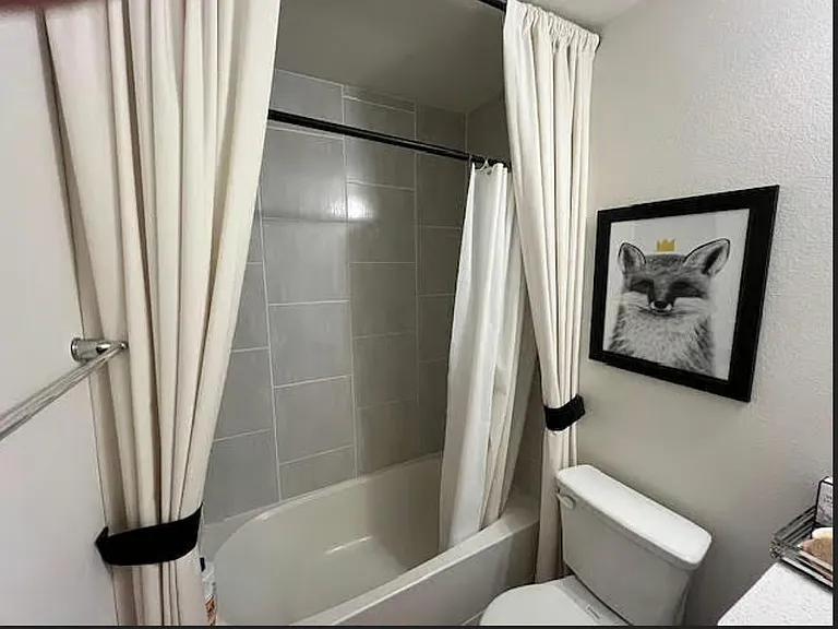 Bathroom features a tub/shower combo with tiled surround, curtain set, and space for everyday toiletries and essentials.