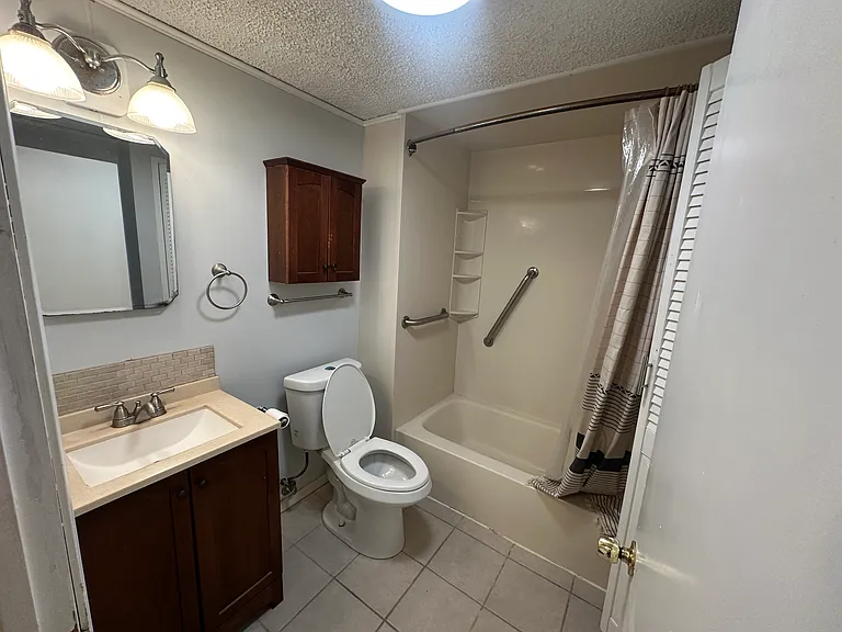 Bathroom with full tub/shower, ventilation fan, vanity, mirror, and towel bars.