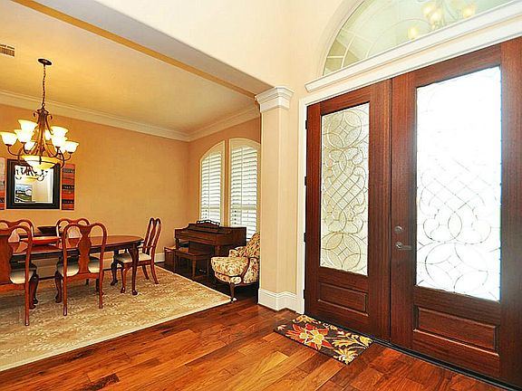 Grand 2 story entrance with hardwoods that leads into dining room. Elegant dining room has iron chandelier, double crown molding. Arched windows covered by plantation shutters