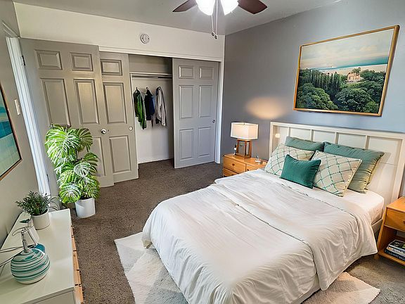 Inviting bedroom with modern ceiling fan, cozy white bed, elegant decor, spacious closet, and lush indoor plants.