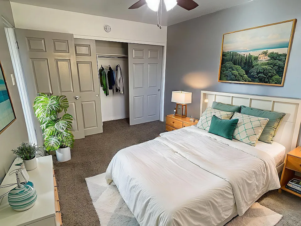 Inviting bedroom with modern ceiling fan, cozy white bed, elegant decor, spacious closet, and lush indoor plants.