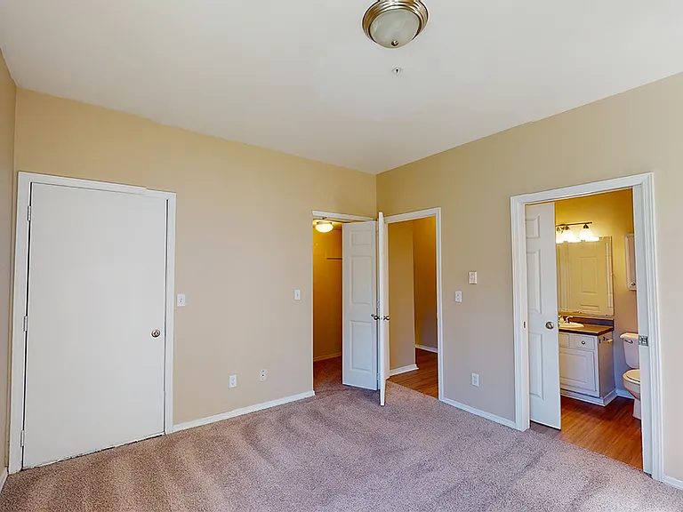 Spacious apartment bedroom with large closet, attached bathroom and plush carpet flooring.