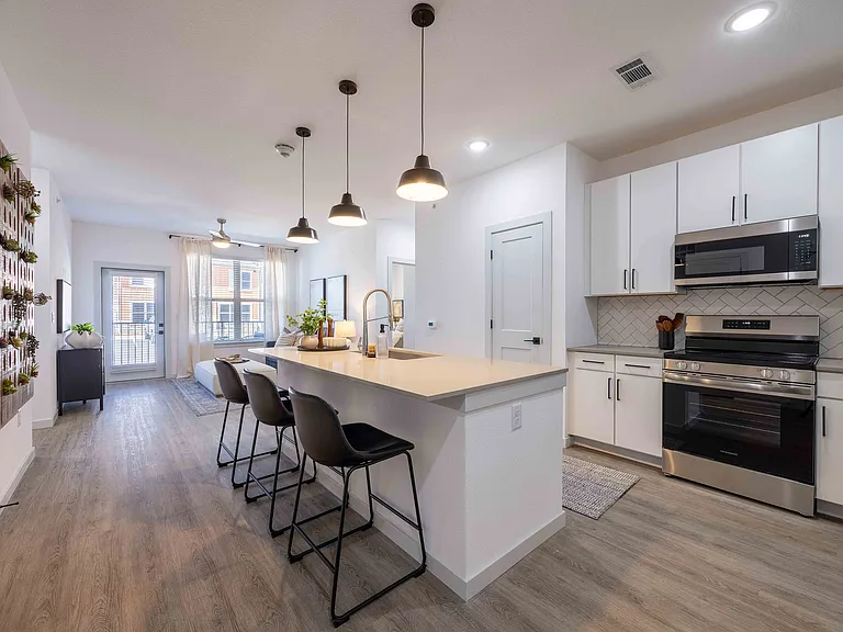 The B1 floor plan kitchen at Garrett Parker includes a quartz island with seating for three, stainless steel appliances, and a herringbone tile backsplash.