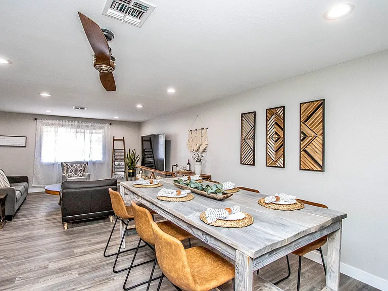 Lovely dining and living area at Casa Del Sol, Tempe rental home. Features a long rustic wooden dining table with stylish leather chairs, geo wall art, and an open layout flowing directly into the main living room space. Prime Tempe, AZ rental.