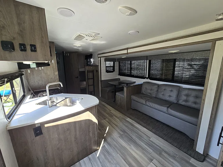 Open-concept living area with a built-in sofa, dinette, and adjacent kitchenette featuring a double sink and counter space.