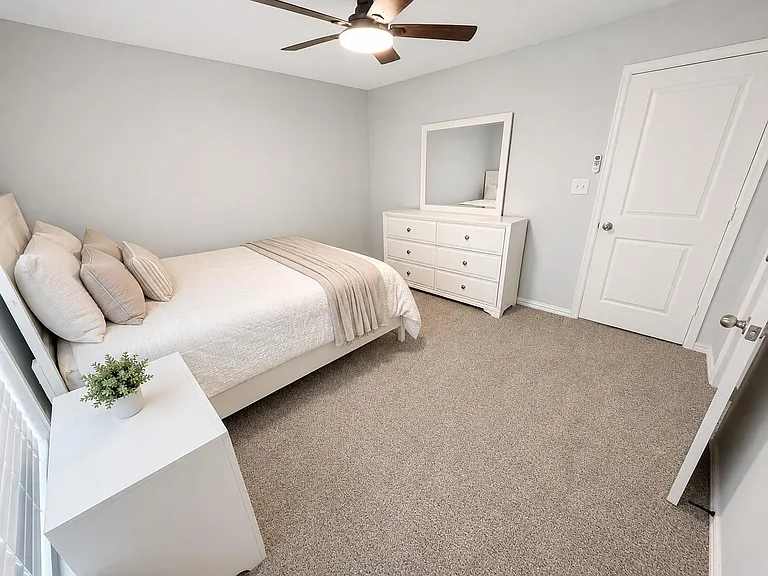 Well-appointed bedroom with a full bed, dresser with mirror, plush carpet, and ceiling fan for year-round comfort.