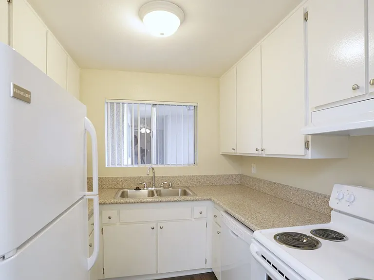 Kitchen with white appliances including refrigerator, dishwasher, and electric range at Villa Pacific Apartments in Oceanside, California.