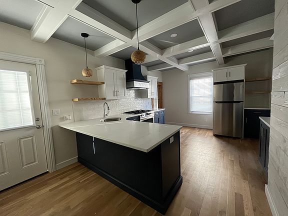Kitchen with seating for 3 at the Peninsula. Floating Shelves, Pendant Lighting and Custom Built Range Hood. Also included is shelving for cook books and a Microwave to the right of the refrigerator.