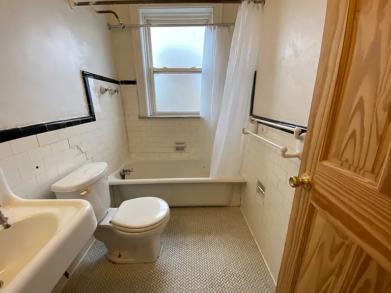 This bright bathroom features original tilework, a full-sized tub, and a frosted window that provides privacy while allowing sunlight to fill the space.