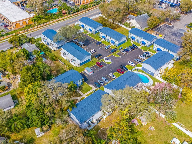 Charming aerial view of a vibrant apartment complex featuring bright blue roofs, lush green spaces, and a community pool, offering a perfect blend of comfort and convenience.