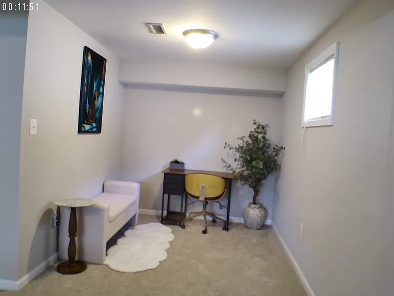 Carpeted flex space with a dedicated desk nook, overhead lighting, and a window for natural lightideal for a home office.