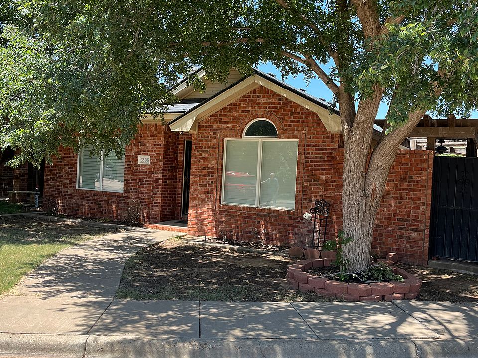 Front view of property with large shade tree and side private gated patio