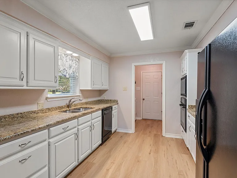 Kitchen featuring white cabinetry, granite countertops, stainless steel double basin sink, and wood-finish flooring