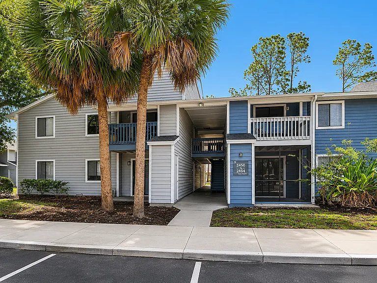 Charming blue and gray apartment building with lush landscaping and palm trees, inviting entrance, and balcony views.