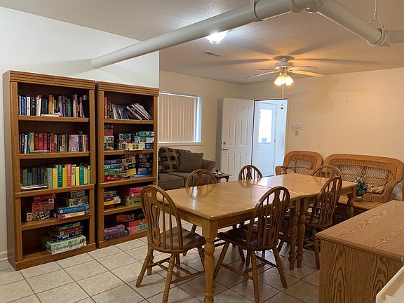 Community room has a table, couch, kitchen and bookshelves with books, games and puzzles.