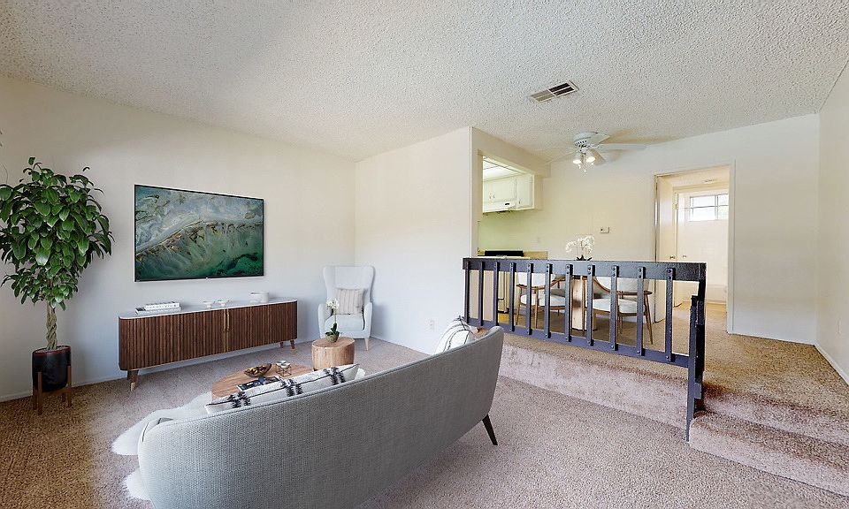 Staged living room with carpet, work-from-home area, and stairs to dining area, and galley kitchen.