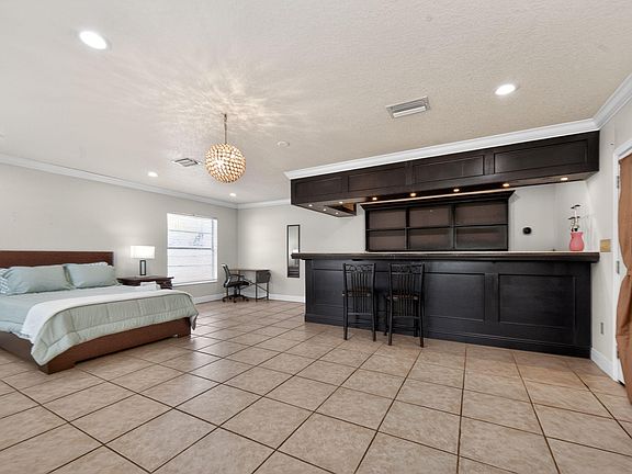 Spacious studio-style bedroom with tile flooring, a work desk, and a built-in bar with seating for dining or entertaining.