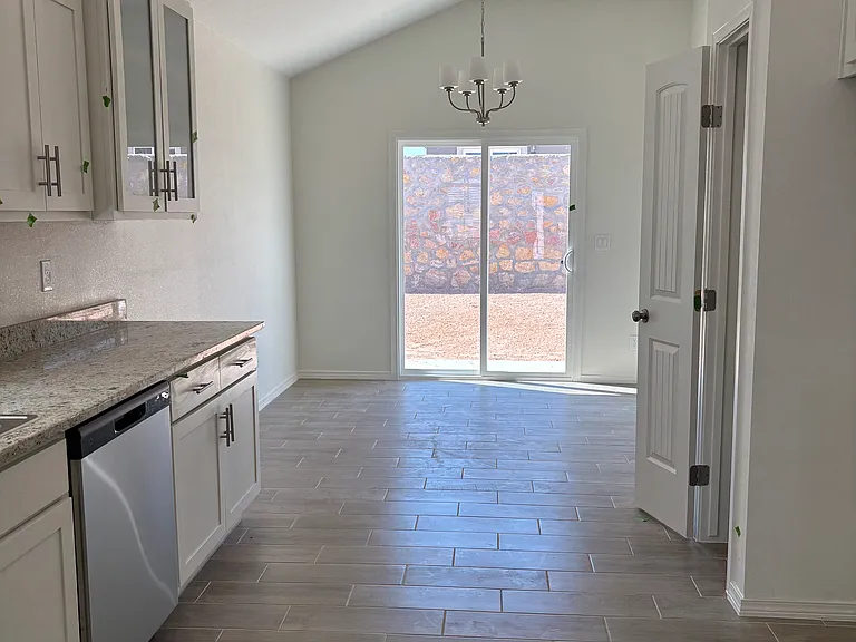 Open-concept kitchen and dining area featuring granite countertops, stainless steel appliances, abundant natural light, direct access to the backyard, and newly installed privacy window tint for added comfort and energy efficiency.