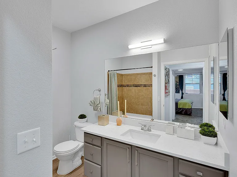 Modern bathroom with elegant vanity, large mirror, and view into a cozy bedroom. Features neutral colors and stylish decor.