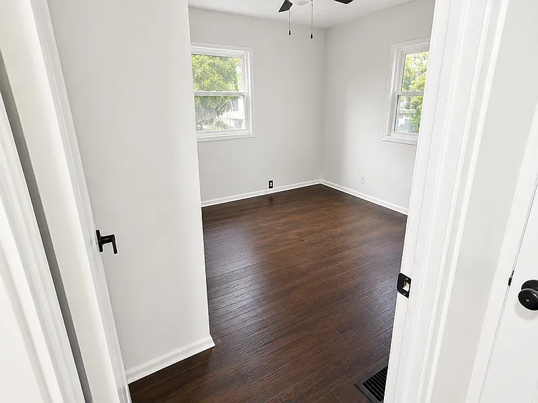 Bright bedroom with hardwood flooring, natural light, and ceiling fan.