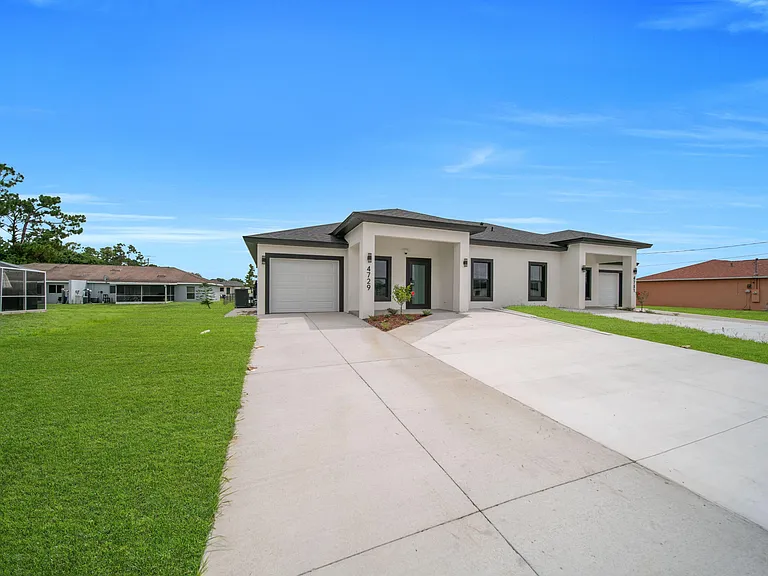 Contemporary single-story exterior with a wide concrete driveway, attached garage, and covered entry with front lawn.