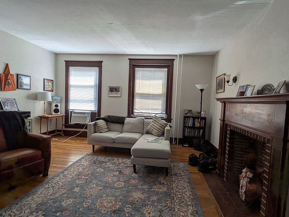 Large living room with huge windows overlooking Main St with an ornamental, original fireplace