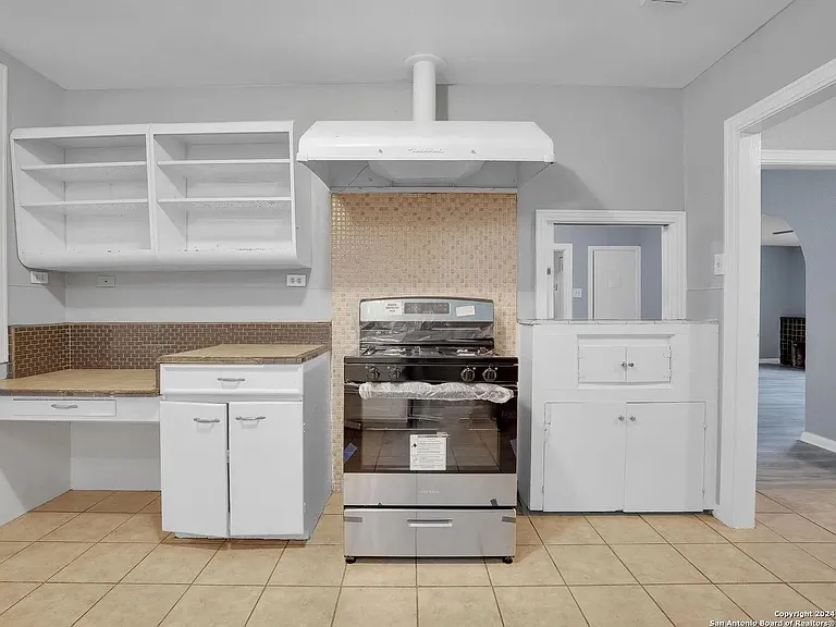 Kitchen features a freestanding range with vent hood, tile backsplash, ample open shelving, and generous counter space.