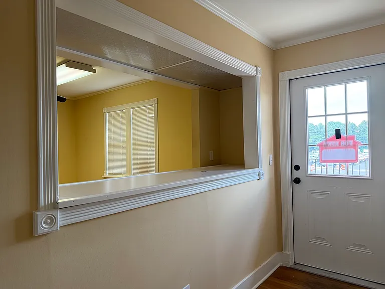 Entryway with glass-paneled door and pass-through window, connecting to warm interior reception area.