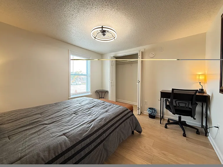 Furnished bedroom with a full bed, work desk, and closet; window light and durable flooring for easy upkeep.