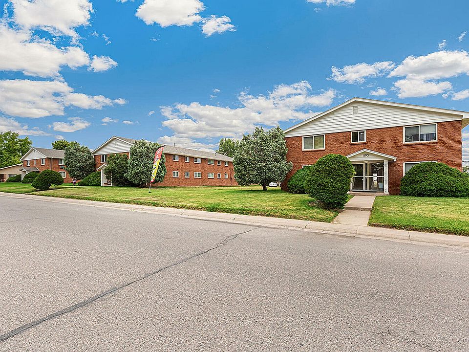 Charming brick apartment buildings with well-maintained lawns and vibrant greenery under a clear blue sky.
