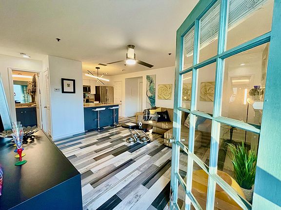From patio looking into living room with kitchen in foreground along with unit entrance to the right of kitchen. To the right of the refrigerator is door to laundry closet with full size stacked W/D. Left foreground is bathroom.