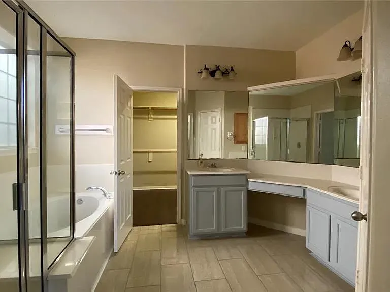 Spacious bathroom with dual-sink vanity, large mirrors, and a soaking tub/shower combo plus a walk-in closet for storage.