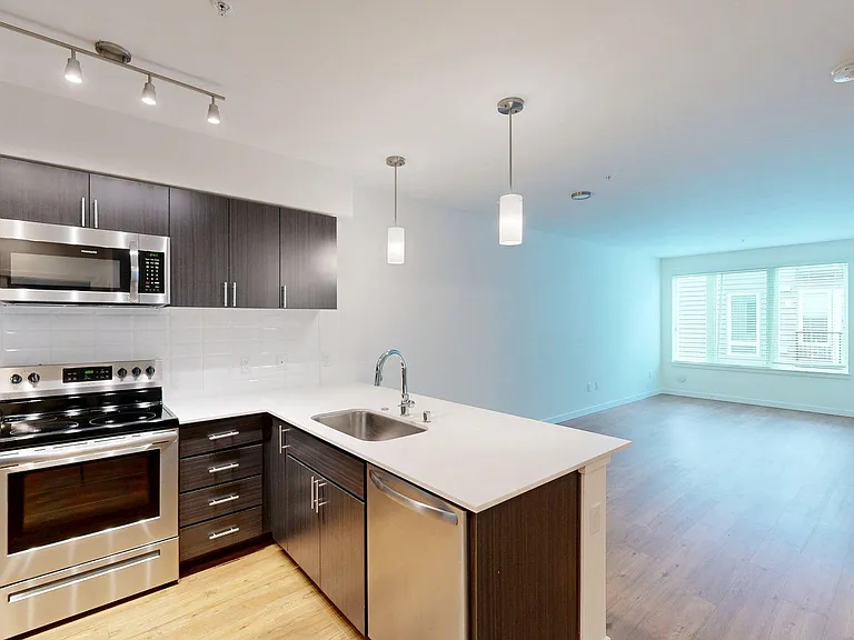 Apartment kitchen with stainless steel appliances, light counters, and wood style floor.