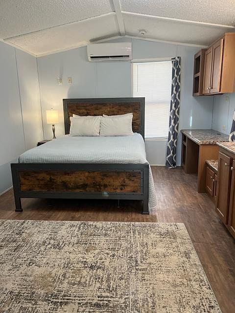 Bedroom with queen bed, nightstand, desk area, minisplit for AC and heat, two windows and soft rug.